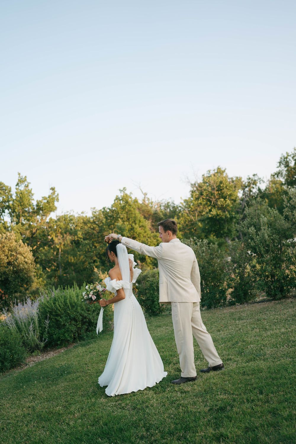 La mariée et le marié dansent à l'extérieur sur une pelouse verte entourée d'arbres luxuriants lors de la célébration de mariage.