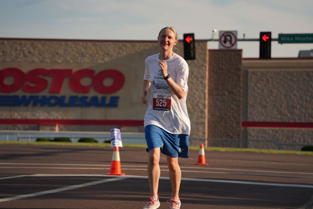 Male runner wearing bib number 325 races past a Costco Wholesale store during an outdoor road race event.