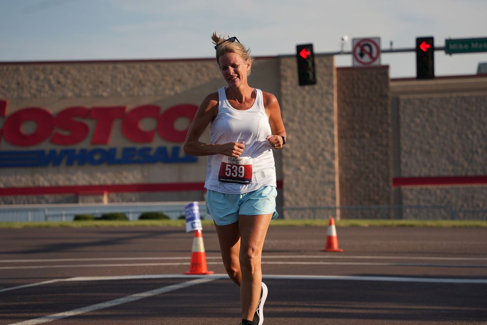 Woman wearing bib 539 running a road race past a Costco Wholesale store on a sunny day.