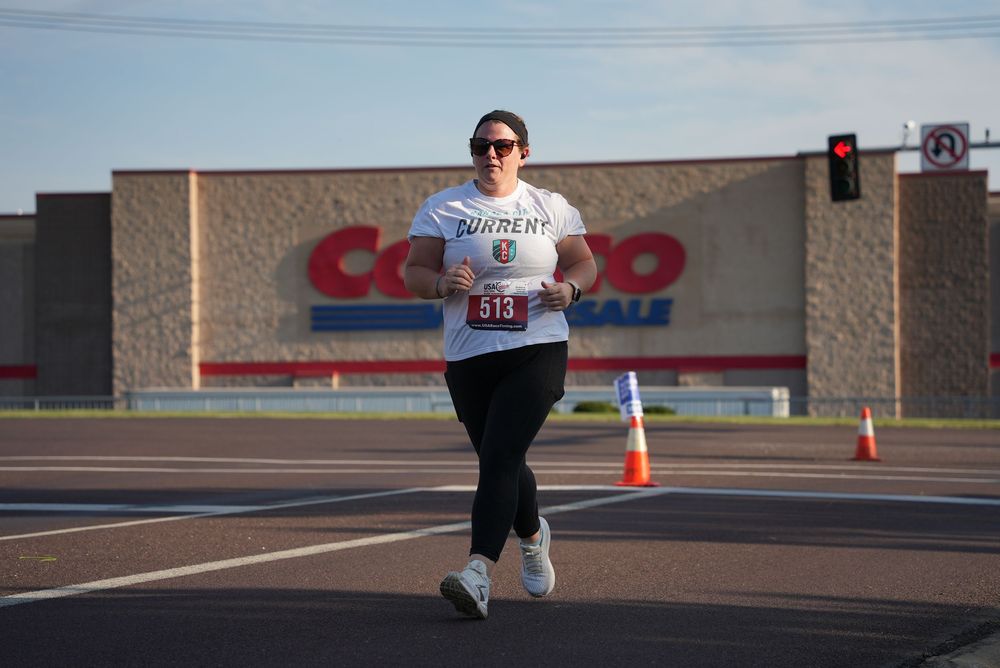 Woman wearing bib number 518 running a race near a Costco Wholesale store with traffic cones and stoplight.