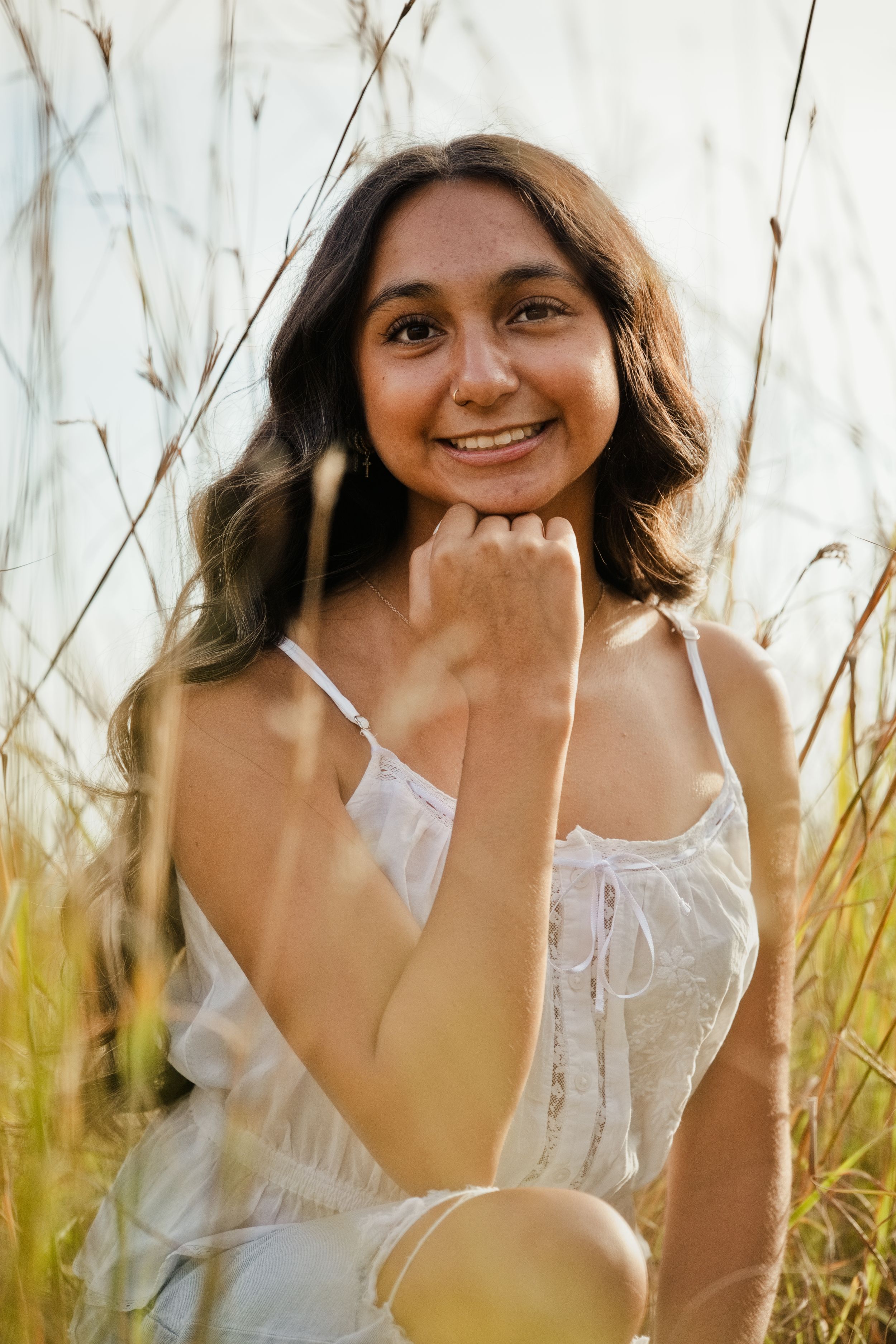 Young woman in white sundress smiling in golden tall grass field, portrait photography.