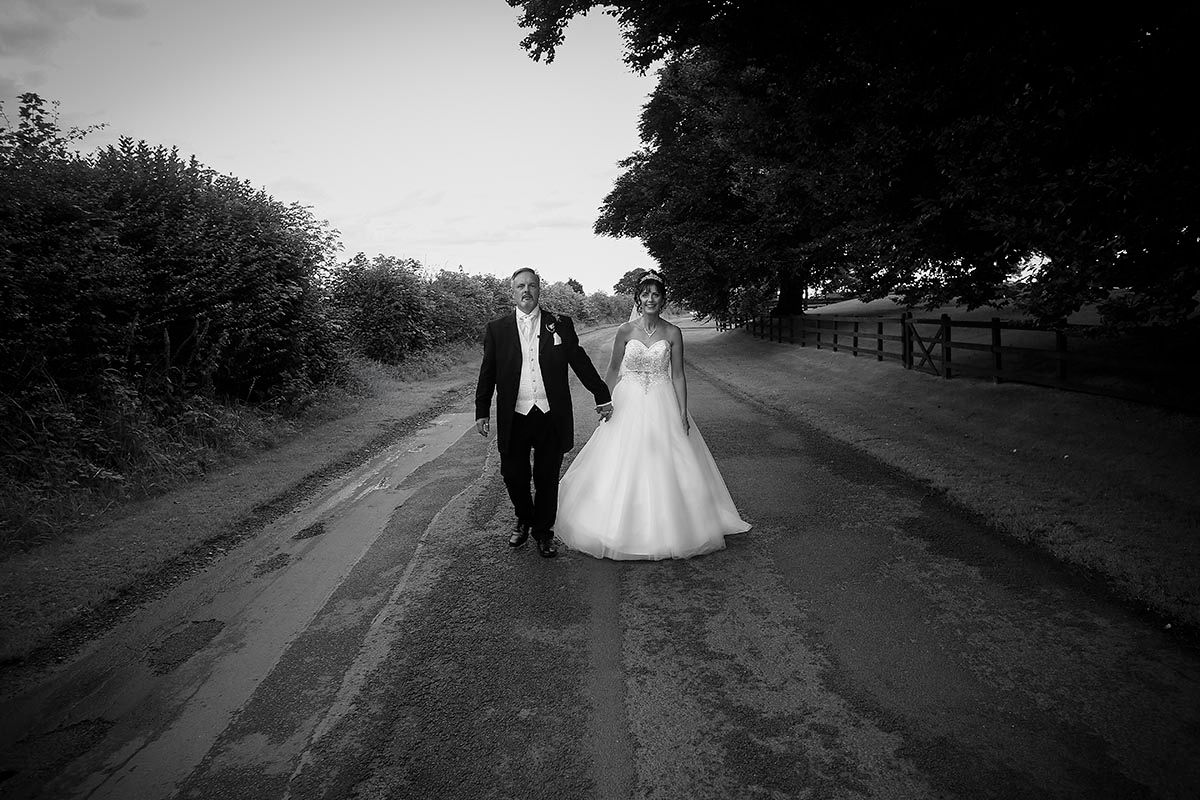 Black and white photo of a bride and groom holding hands walking down the road outside Skitby House wedding venue