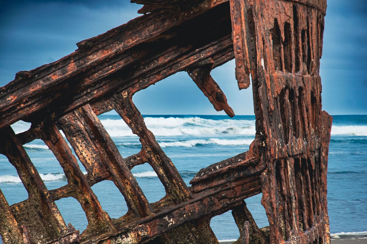 Rusty shipwreck remains close-up with ocean waves and blue sky in background on a sandy beach.