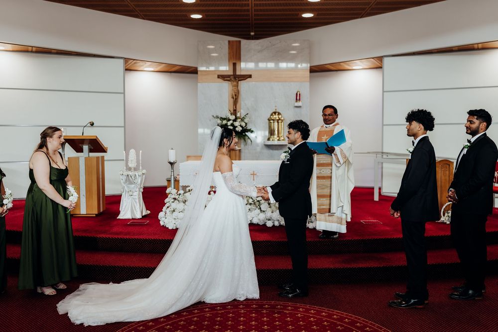 Bride and groom exchange vows at church altar with wedding party in green and black formal attire.