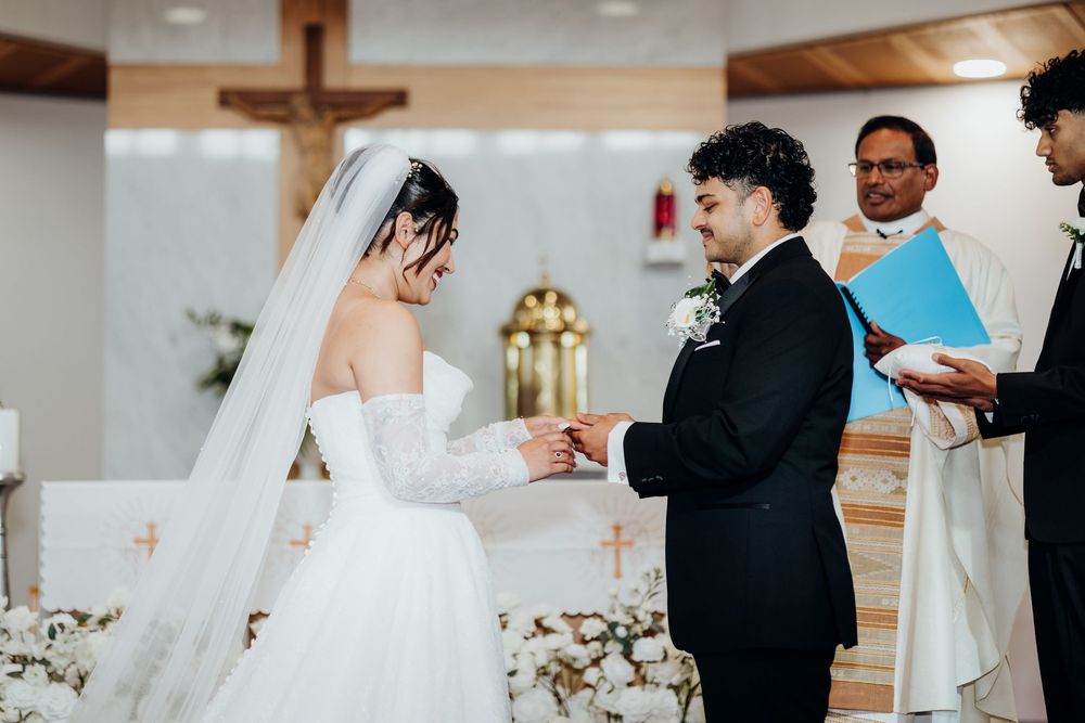 Bride and groom exchange rings during romantic church wedding ceremony with officiant.
