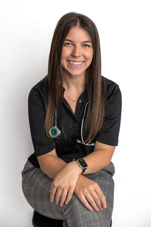 Smiling female healthcare professional with stethoscope wearing black scrubs and plaid pants poses for professional headshot.