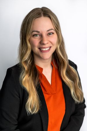 Professional headshot of a smiling woman with long blonde hair wearing an orange top and black blazer.