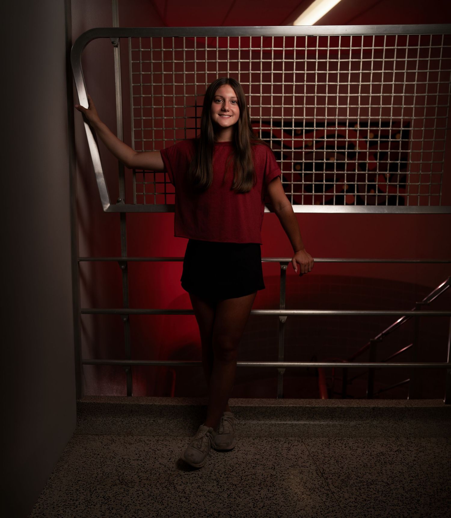 Dramatic senior portrait of a girl in a red top photographed in an urban stairwell