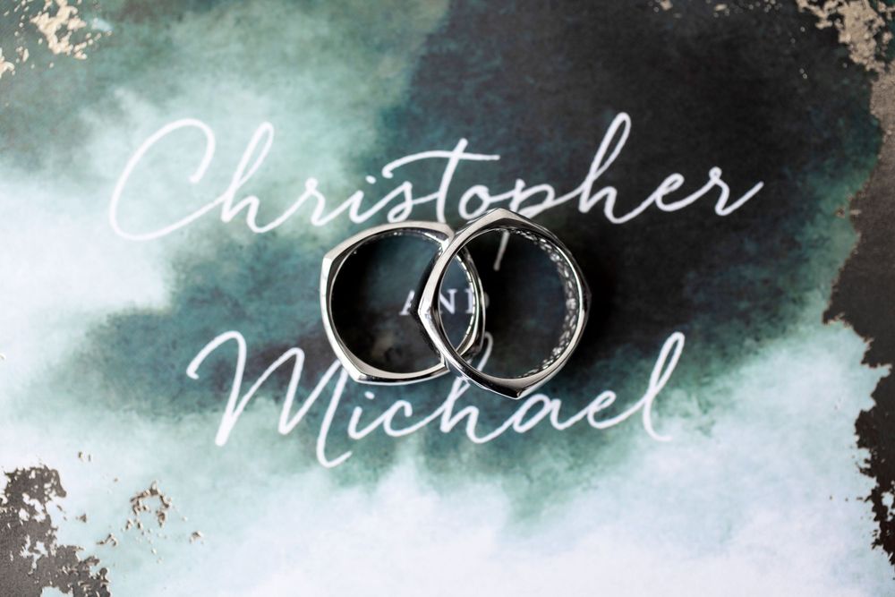Two interlocked silver wedding bands on a teal watercolor background with elegant Christopher Michael script text.