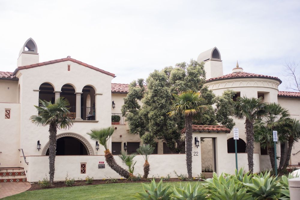 Spanish Colonial Revival mansion with red tile roof, white stucco walls, arched windows, and lush palm trees in a manicured landscape.