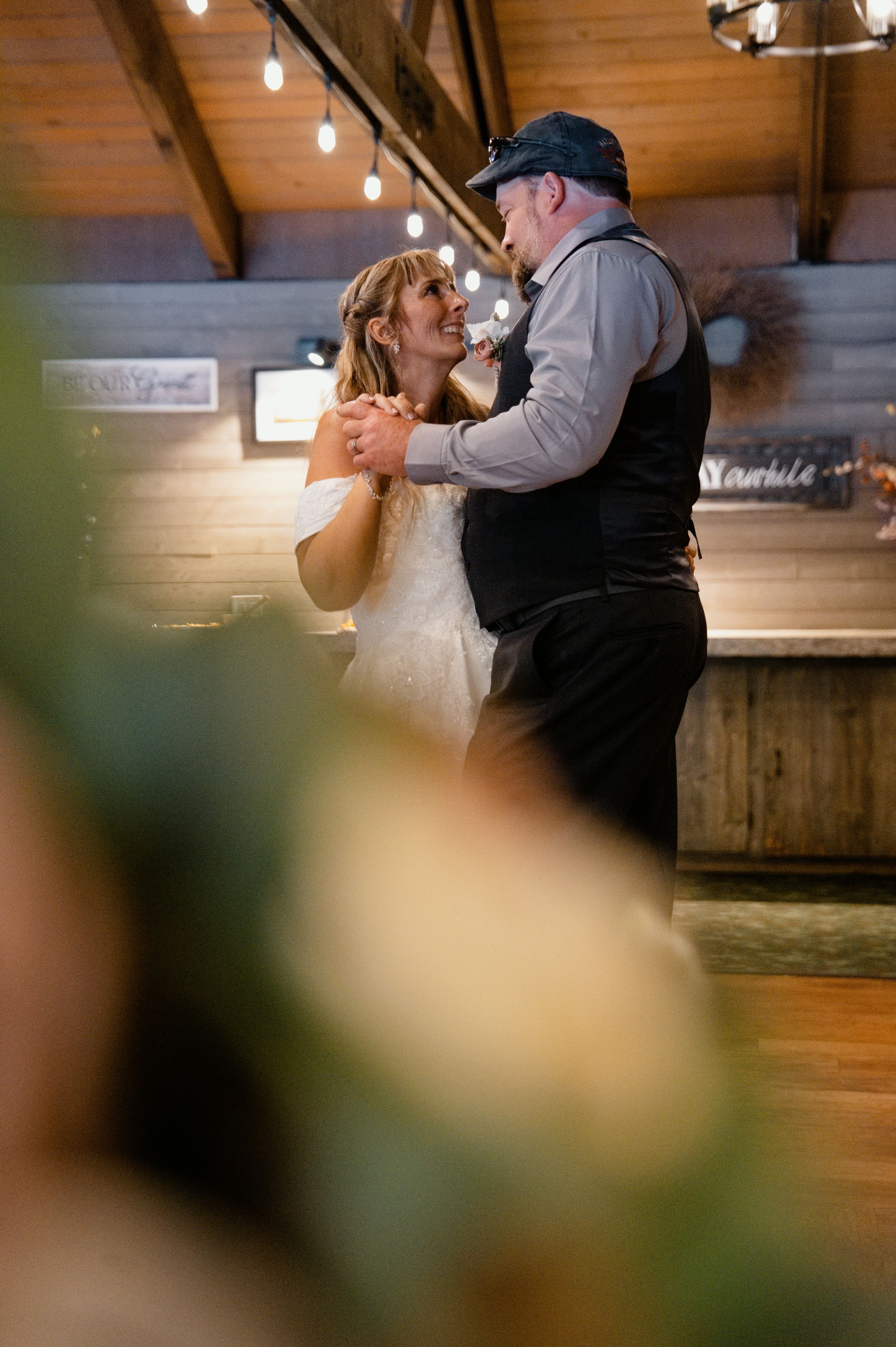 Couple sharing a romantic first dance in a rustic barn wedding venue with warm string lights.