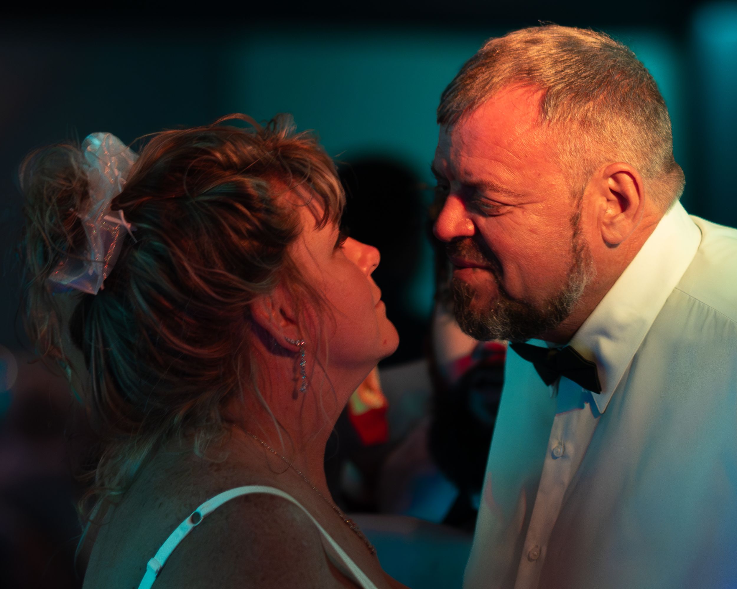 A man in a tuxedo and woman in a blue dress share an intimate moment dancing closely together at a formal event.
