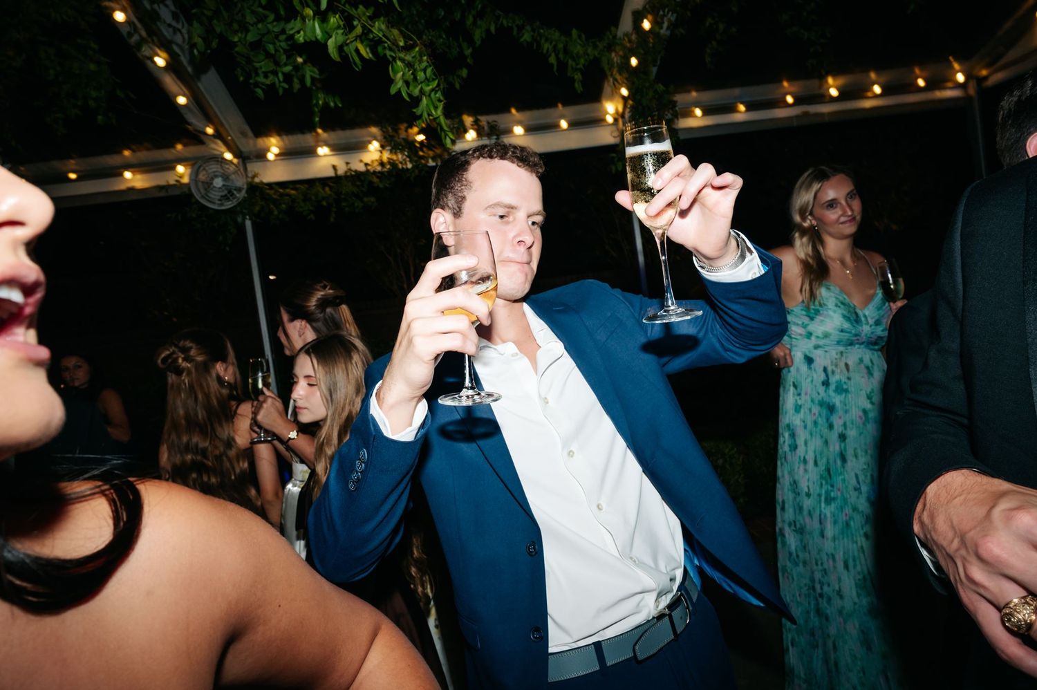 A man holding two champagne glasses dancing during reception at River Oaks Garden Club.