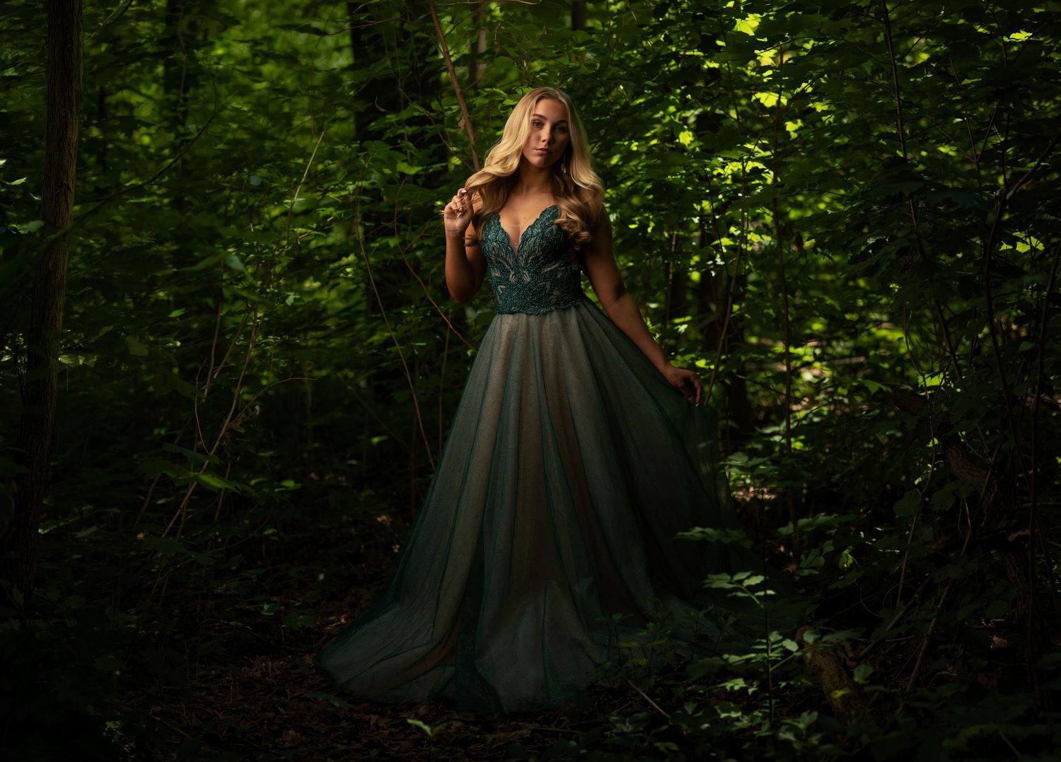 Senior portrait of a girl in a green gown photographed in a wooded setting