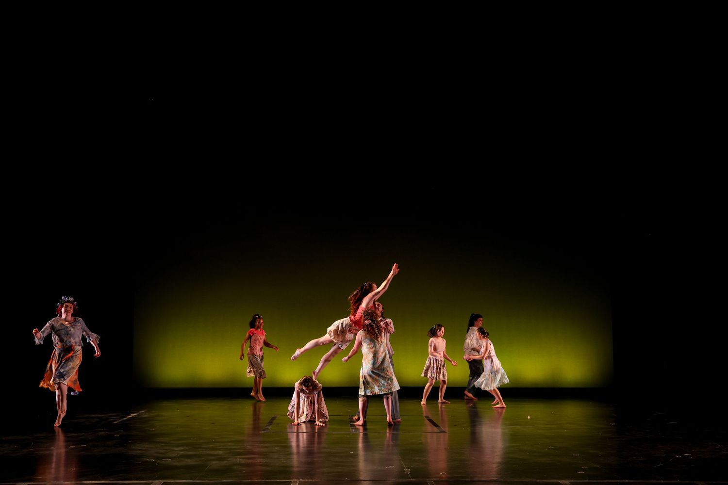 Dancers perform a contemporary dance piece on a dimly lit stage with a green-yellow backdrop.