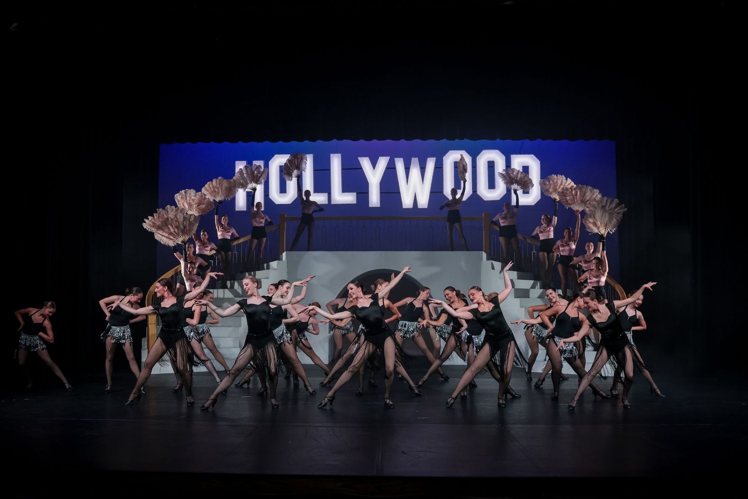 Dancers perform on stage beneath a lit Hollywood sign backdrop in a theatrical dance recital production.