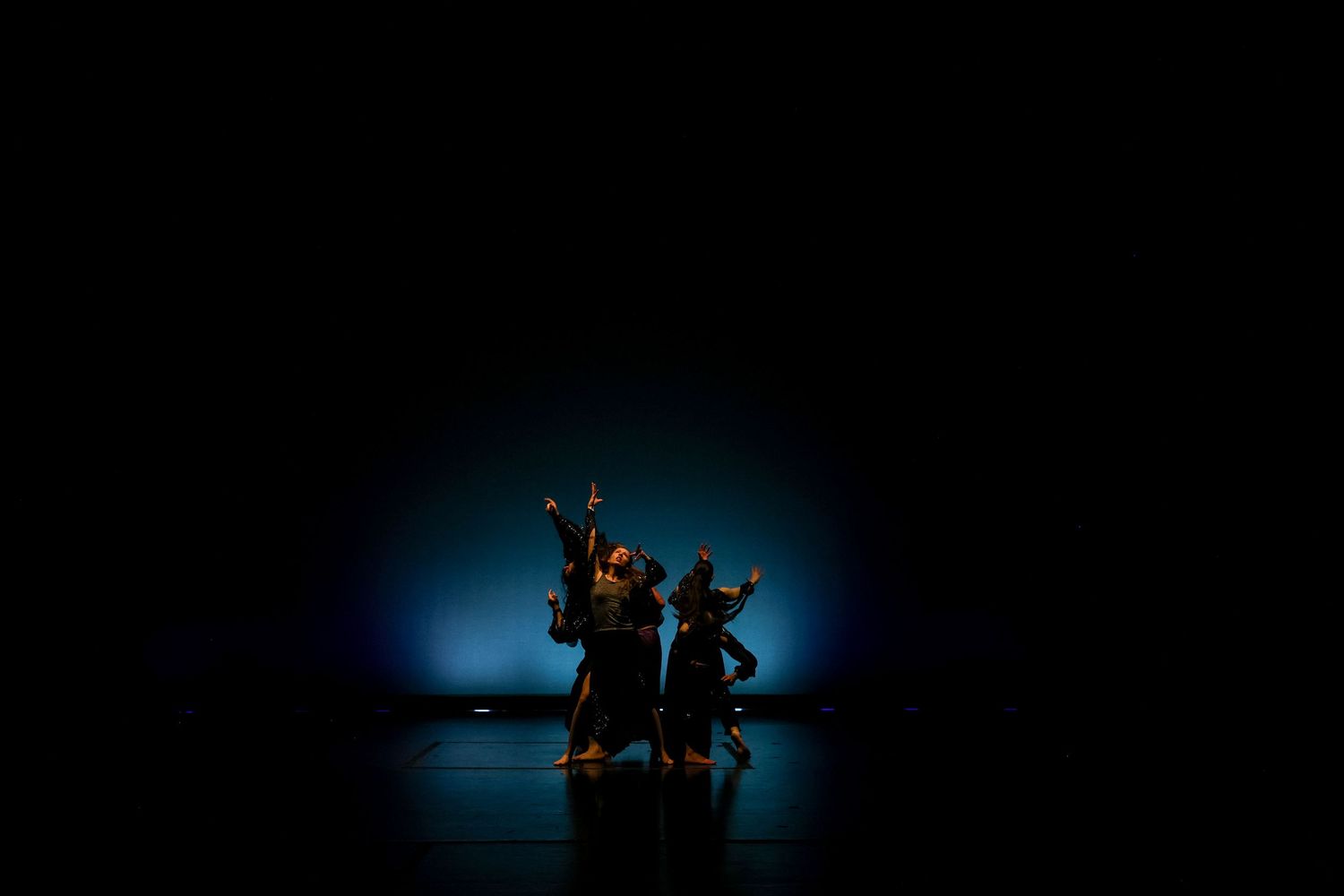 Dancers perform on a dark stage illuminated by a blue spotlight during a contemporary dance performance.