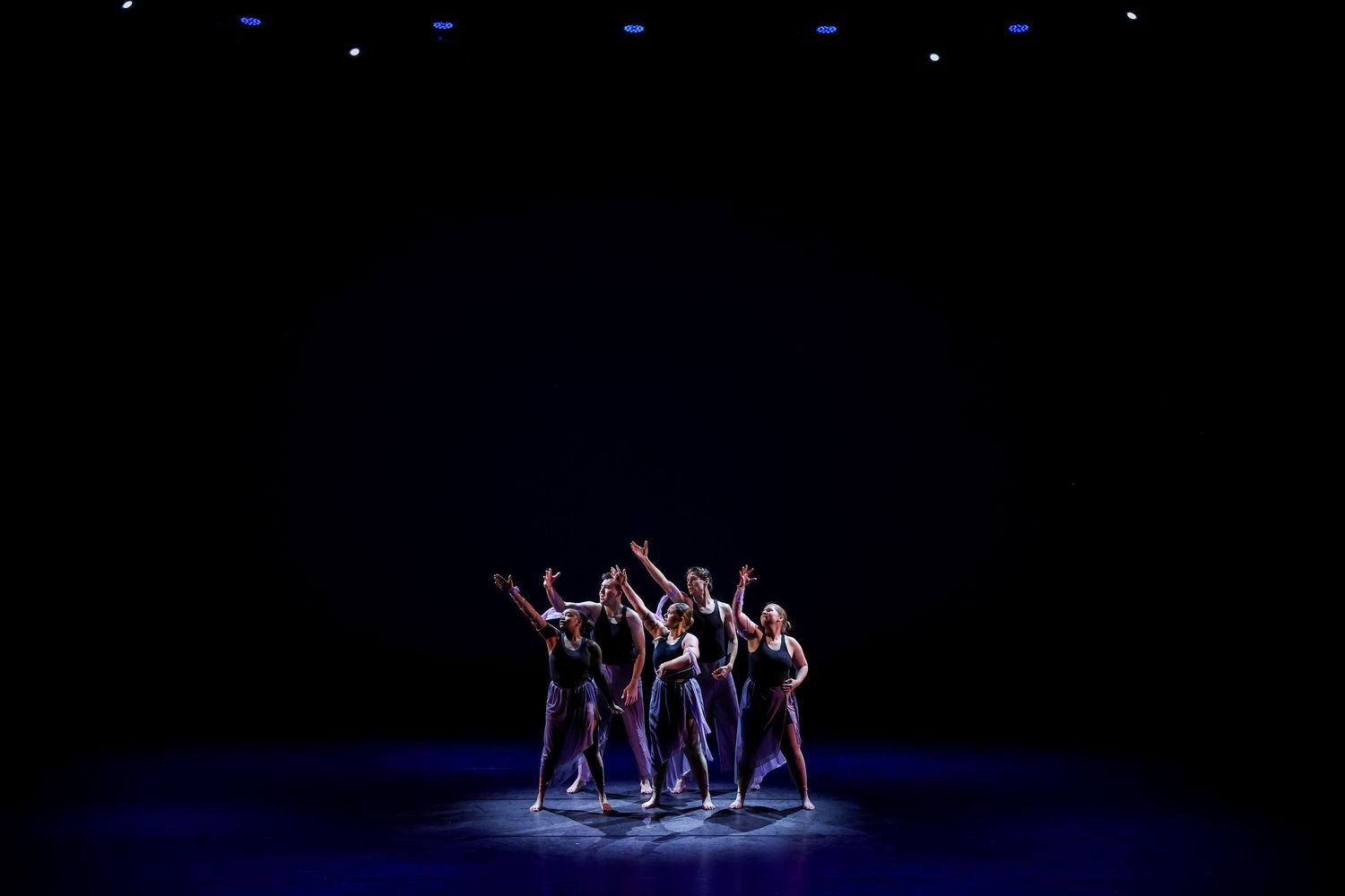 Dancers perform on a dimly lit stage under blue spotlights during a contemporary dance performance.