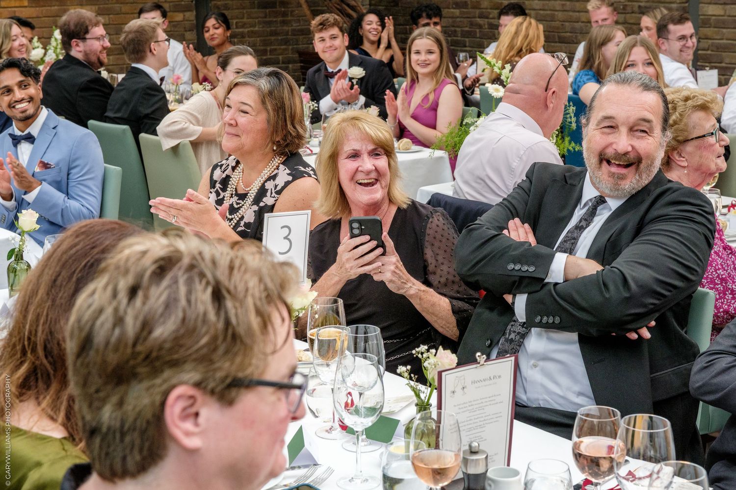 Guests laughing and clapping at a formal gala dinner event, seated at elegantly decorated tables.