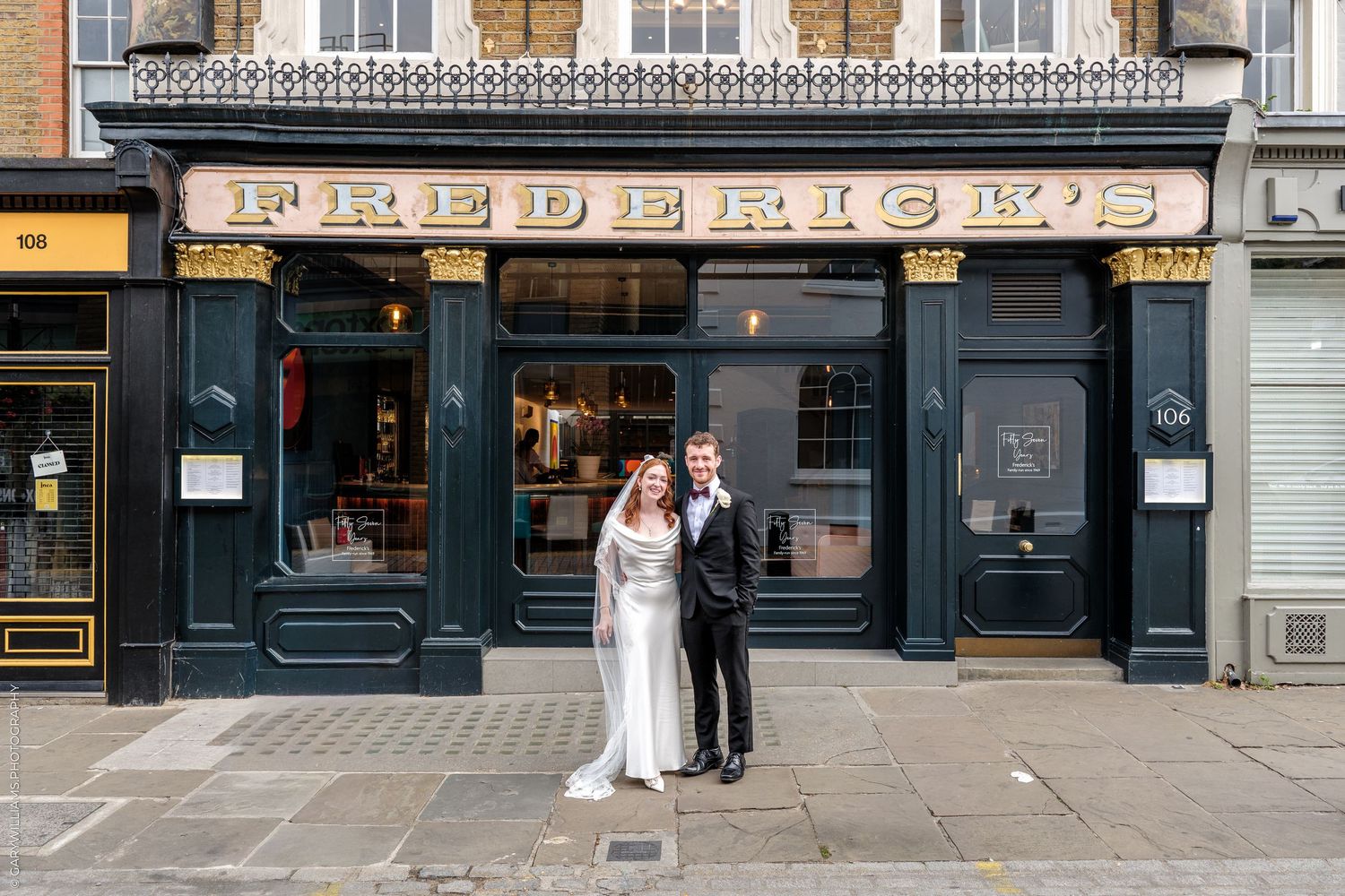 Bride and groom posing outside Frederick's restaurant with dark green facade in London.