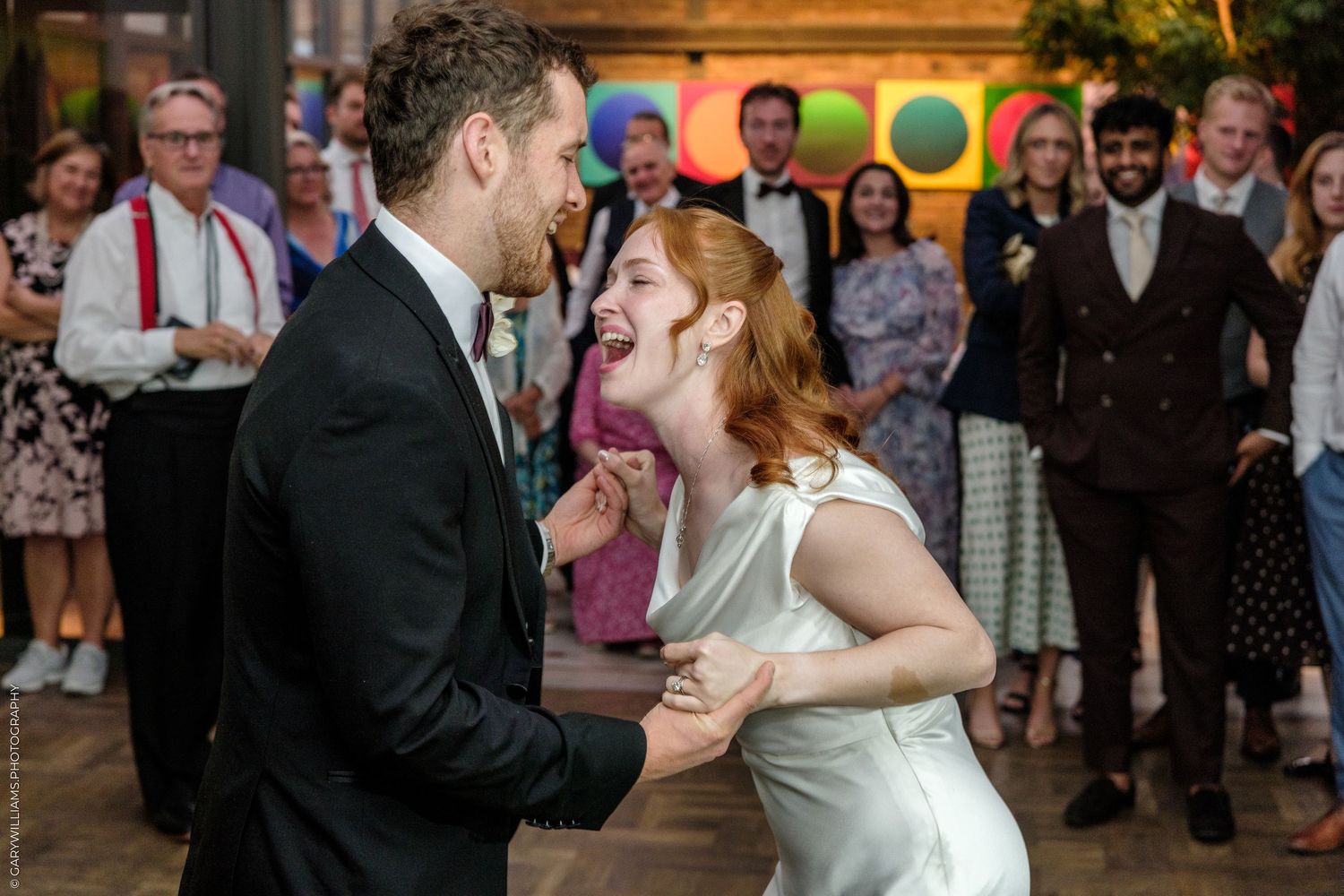Joyful couple sharing first dance at wedding reception with guests celebrating in background.