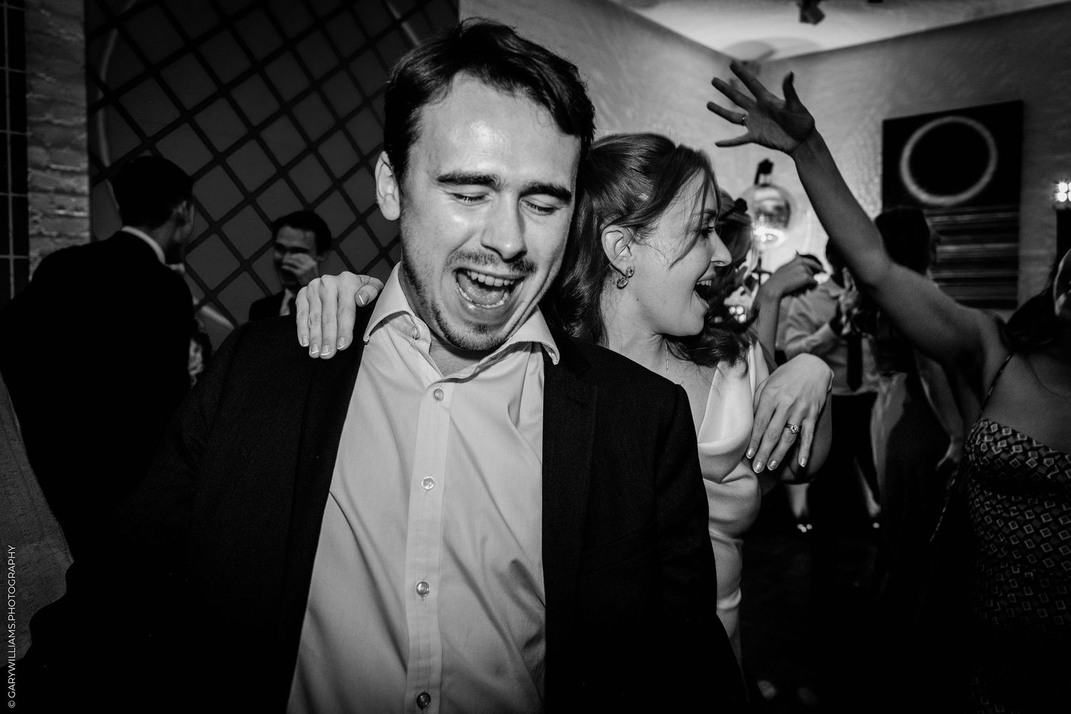 Black and white photo of a joyful man and woman dancing and laughing together at a wedding reception party.