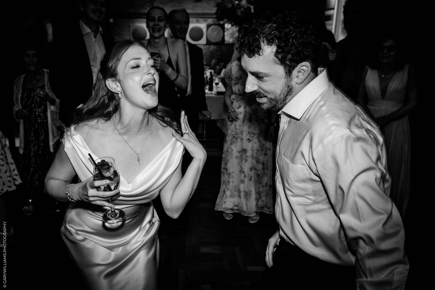 Black and white photo of a laughing bride and groom dancing joyfully at their wedding reception.