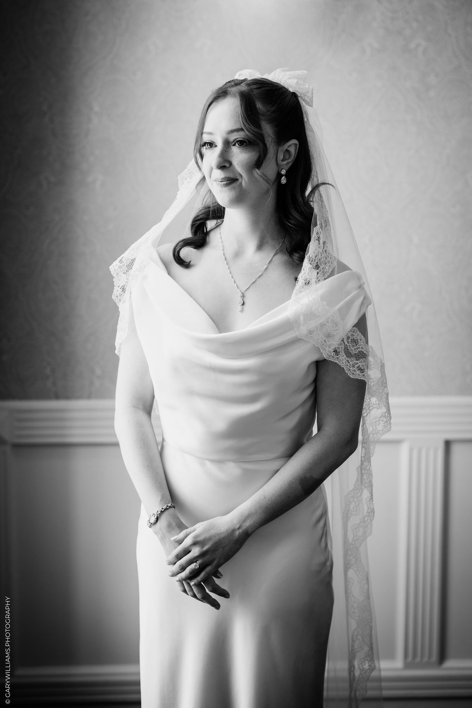 Elegant bride in a white gown and lace veil poses gracefully in a black and white wedding portrait.