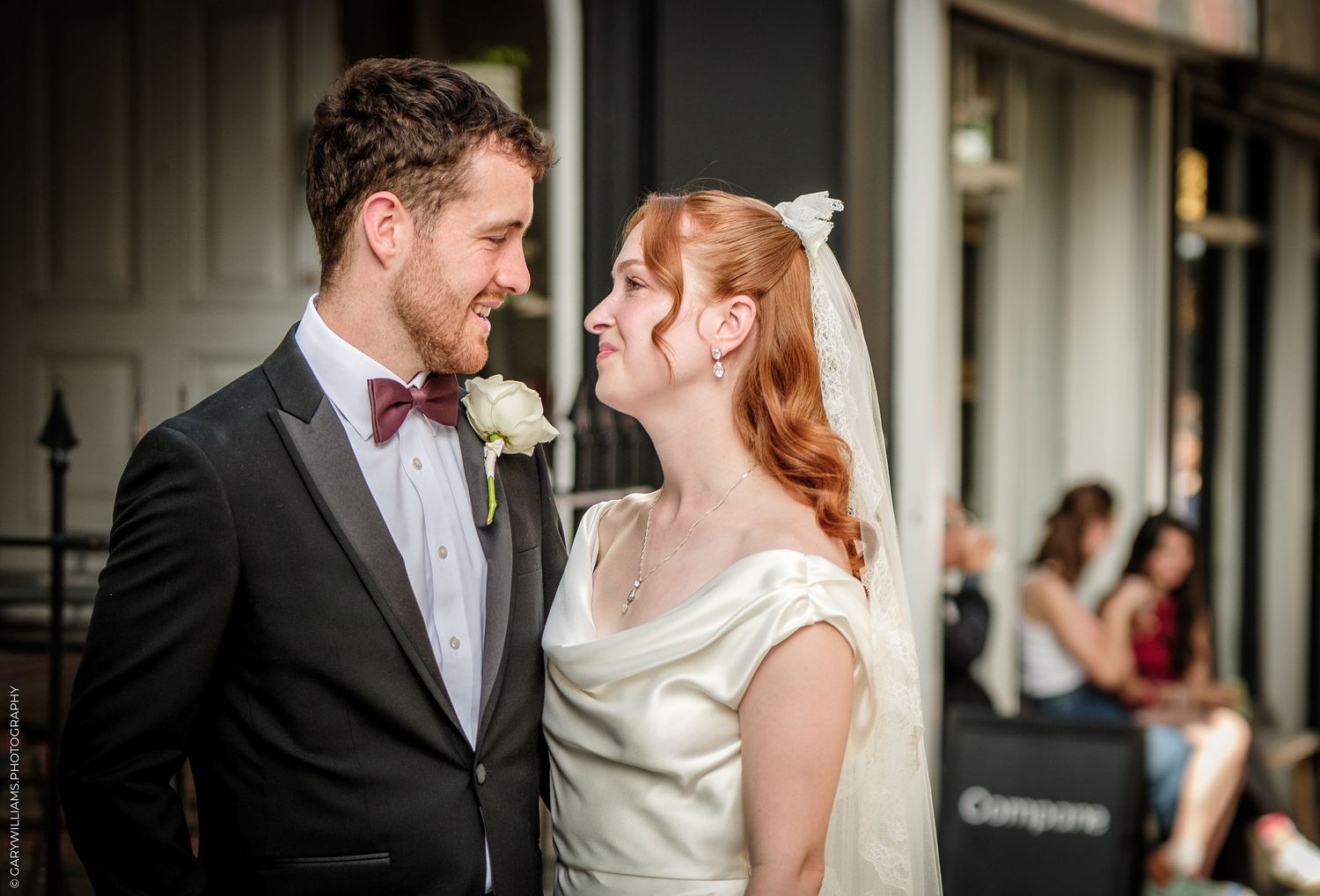 Bride and groom share a romantic moment in wedding attire, smiling at each other outdoors.