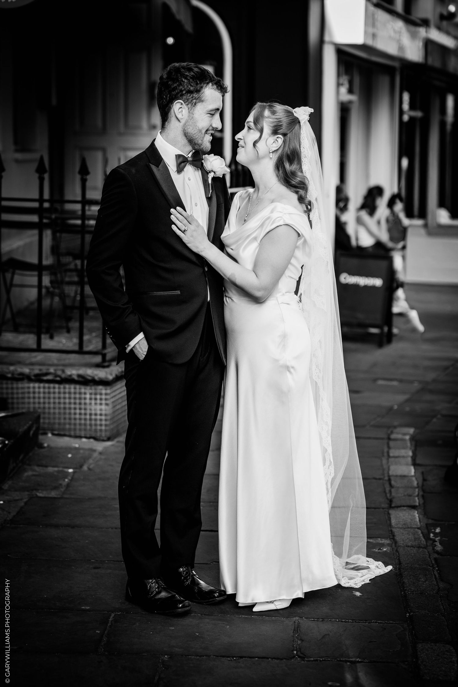 Black and white wedding photo of bride and groom sharing a romantic moment on a city street.