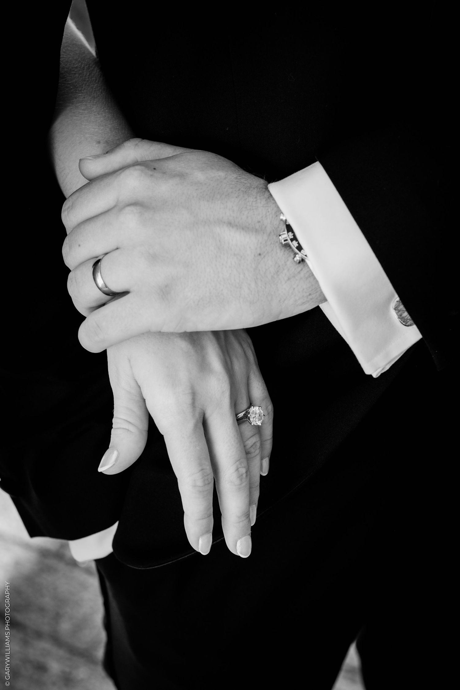 Black and white photo of bride and groom hands showing wedding rings and diamond engagement ring.