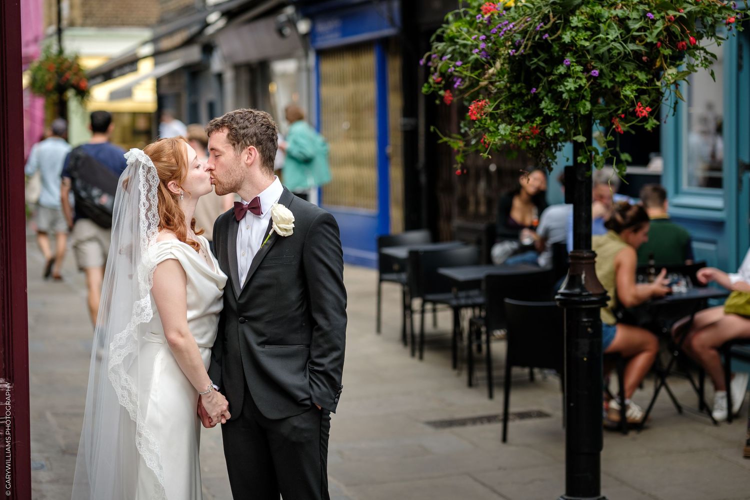 A bride and groom share a kiss on a charming city street, with the bride in a white gown and veil.