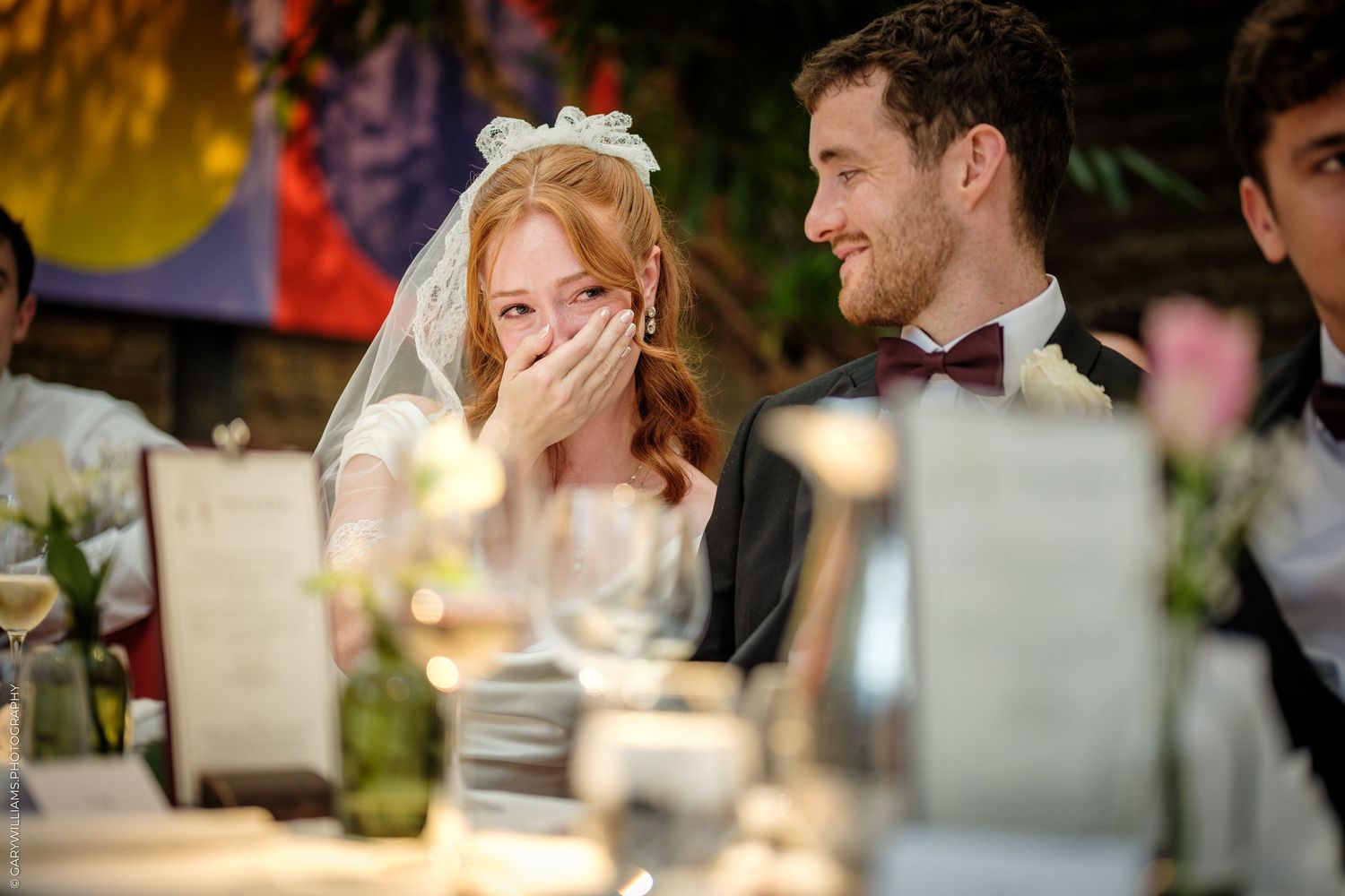 Bride and groom laughing together at wedding reception dinner table with candles and floral decorations.