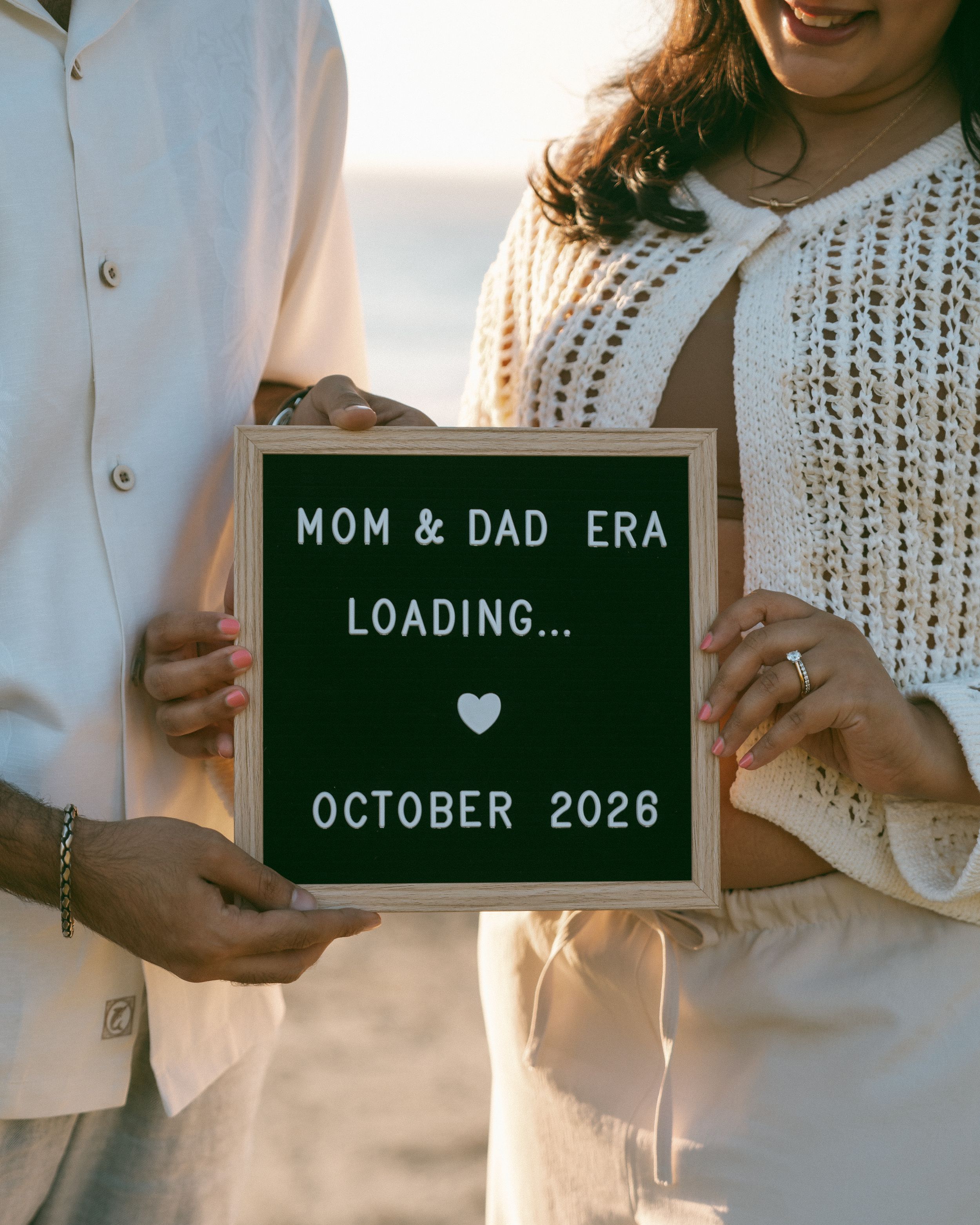 Couple holding a letterboard pregnancy announcement sign reading Mom & Dad Era Loading, October 2026.