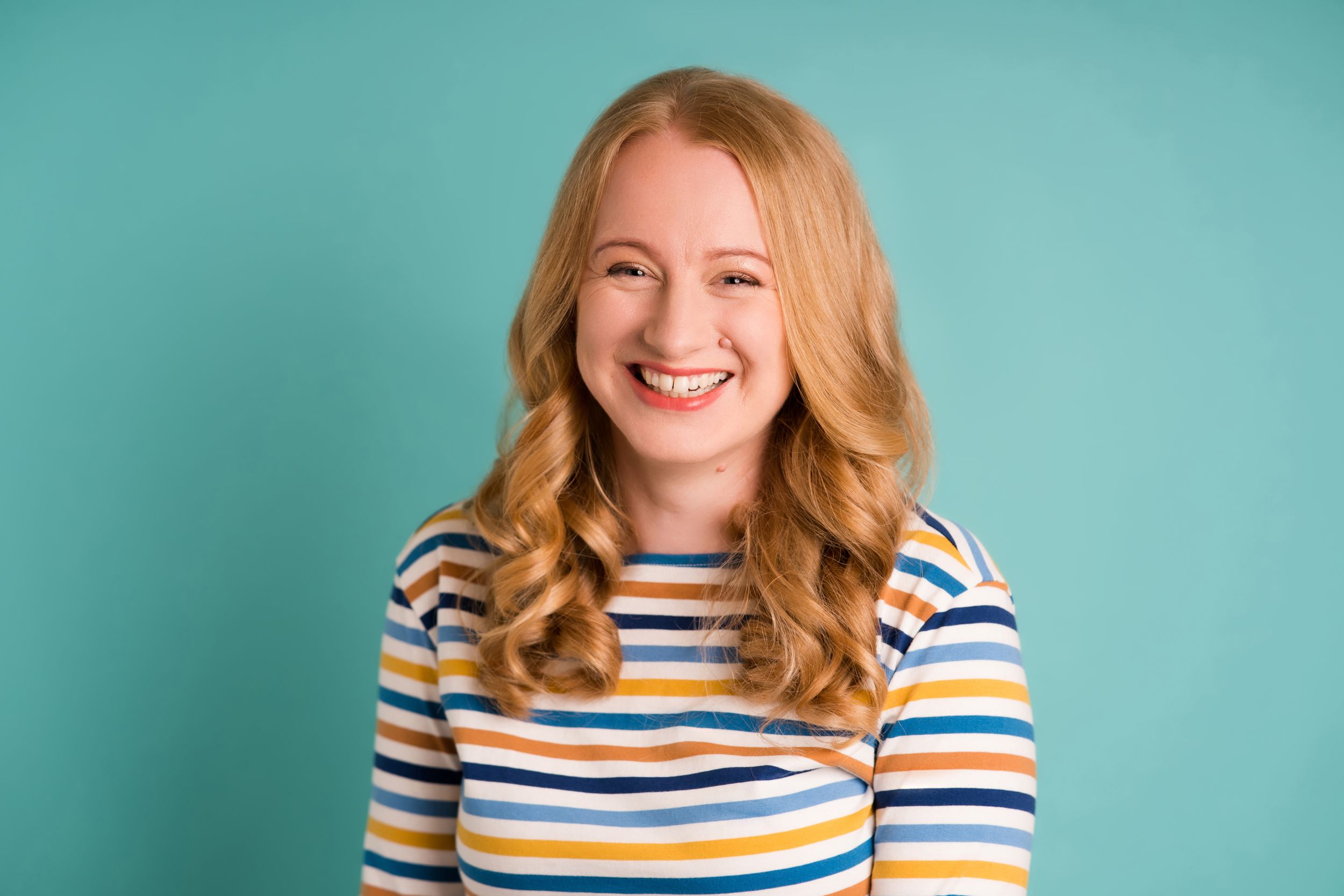 A person in a multi-colored striped sweater smiles warmly against a turquoise blue background.