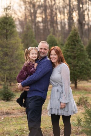 Family poses together among evergreen trees at sunset in a rustic outdoor setting.