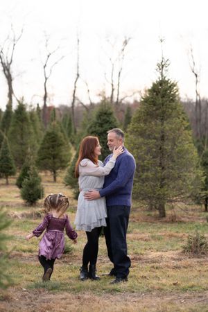 A loving family moment captured among evergreen trees at a Christmas tree farm during golden hour.