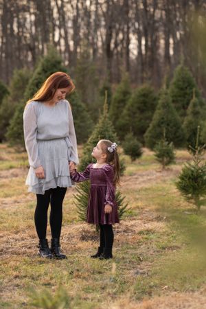 A sweet scene between mother and child walking together through rows of evergreen trees at sunset.