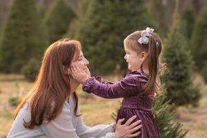 Mother and daughter share a tender moment together at a Christmas tree farm on a sunny afternoon.