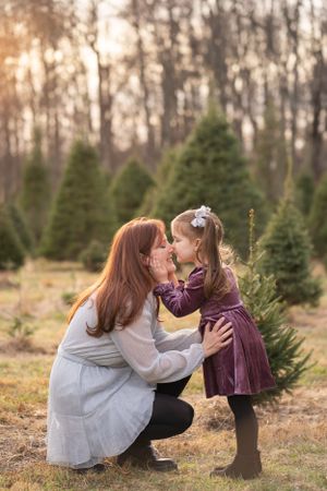 Tender moment shared between mother and child amid evergreen trees at dusk.