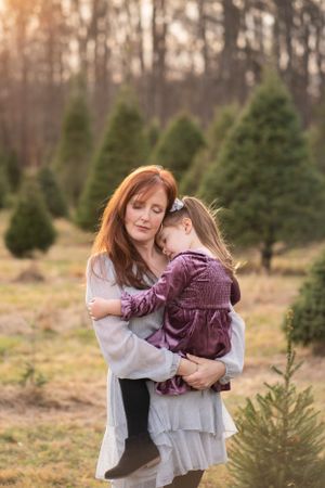 A tender moment between mother and child amidst evergreen trees at sunset.