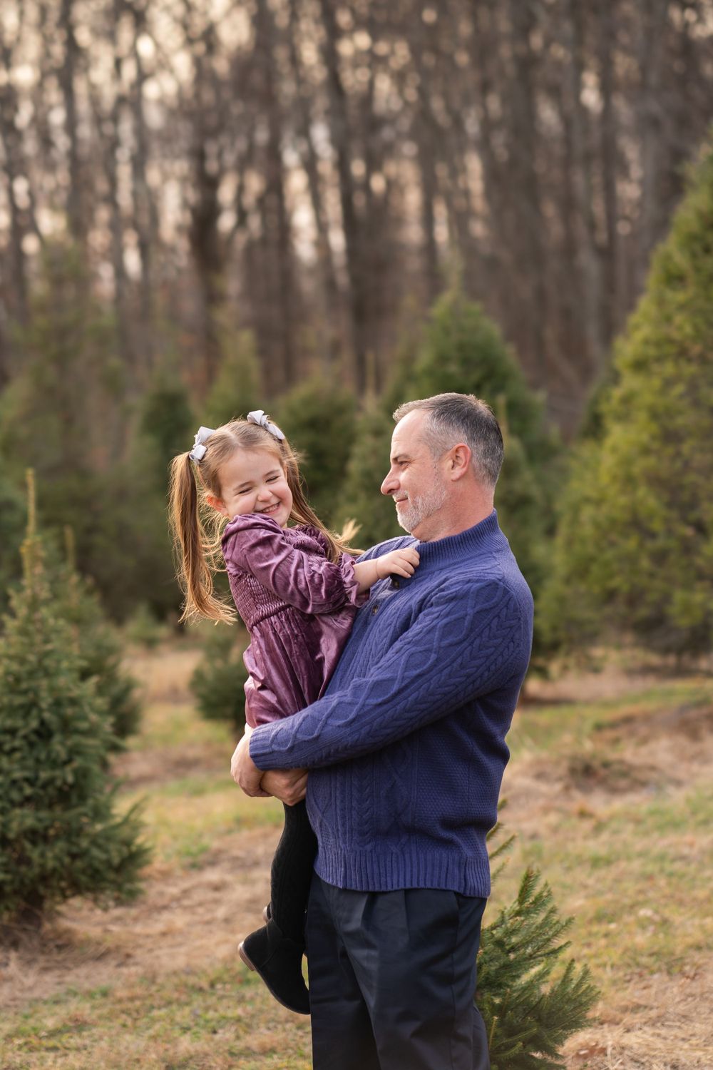 A parent and child share a playful moment together at a Christmas tree farm on a winter afternoon.