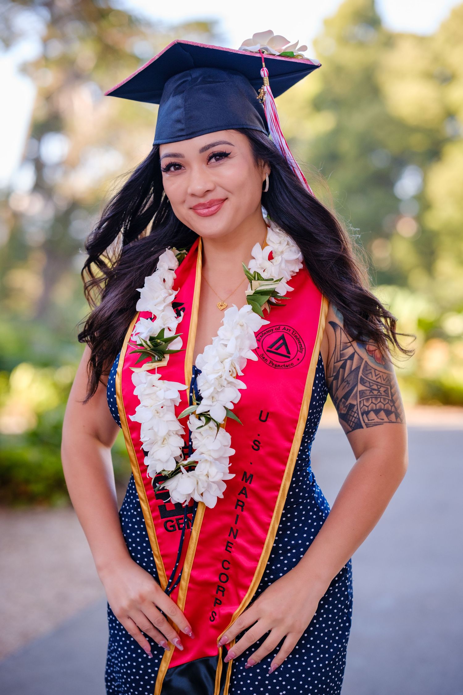 Graduate in purple cap and gown with orange blouse poses in front of turquoise door with Class of 2023 sash.
