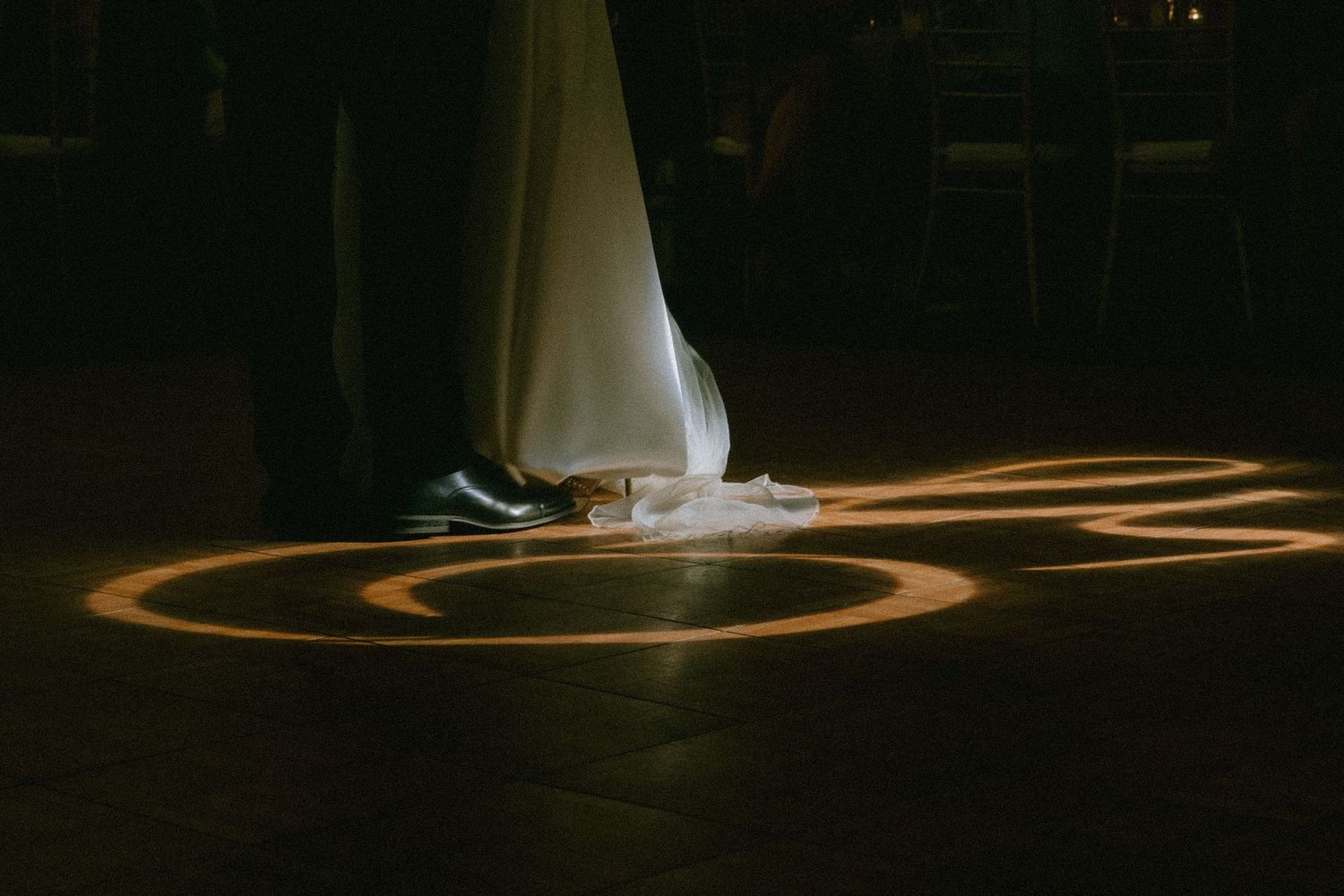 First dance moment with dramatic lighting creating golden circles on dark floor.