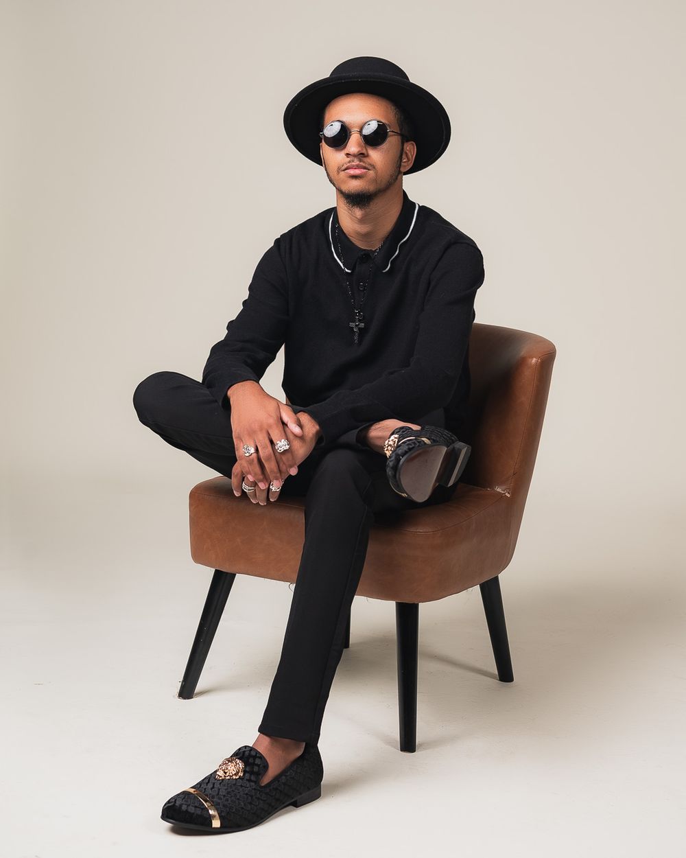 Stylish portrait of someone in all black attire seated on a brown chair.