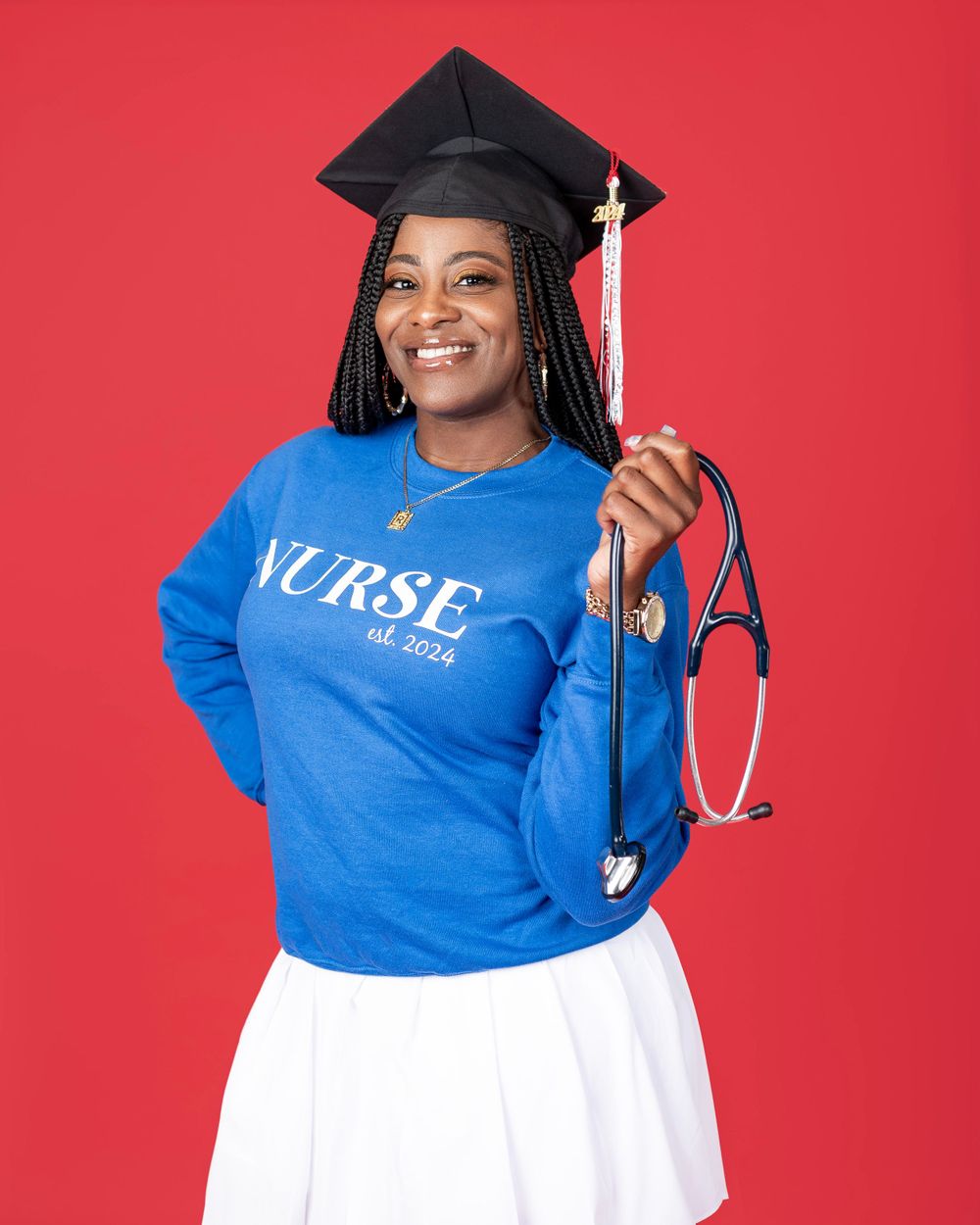 New graduate in blue nursing sweatshirt poses with stethoscope against red background.