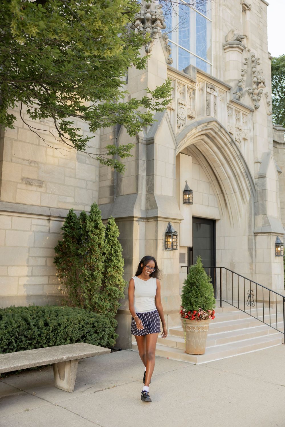 A person walks past a gothic stone church entrance with decorative arches and elegant potted plants along the steps in Birmingham michigan