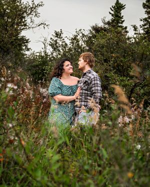 A couple shares a tender moment together in a field of tall grass and wildflowers during golden hour.