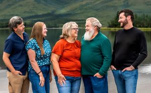 Group of people standing in a row outdoors with mountains and greenery in the background.