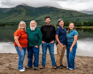 Group of people standing together on a beach with mountains and lake in the background.